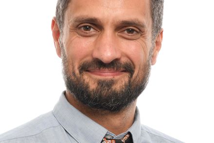 Headshot of Dr Omid Halse smiling, background is pure white, he is wearing a tie with the Charing Cross Hospital Medical badges on it
