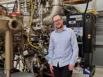 Jordan Alexander-Passe, IROP student at Cornell University standing in front of a large machine in the lab