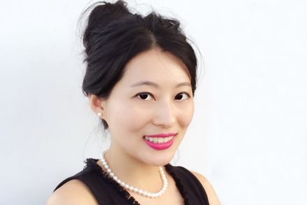 Headshot of Vivien Zhang against white wall - she has her arms folded and hair up