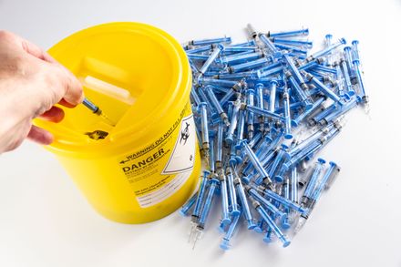 A needle being safely disposed into a yellow clinical waste bucket