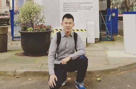 Hang Guo kneeling in front a Imperial College London sign