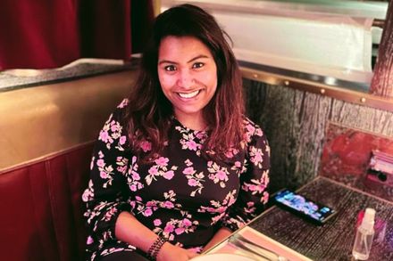 Photo of Sarah sitting at a table in a restaurant smiling at the camera