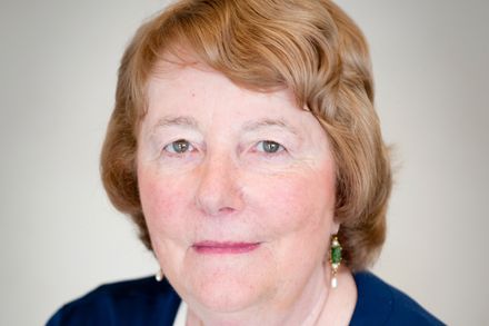 Headshot of Professor Monique Frize against a beige background. She is wearing a navy cardigan and a necklace with a pendant.