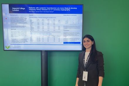 A picture of student Eleni Tserioti standing in front of a digital display of her presentation