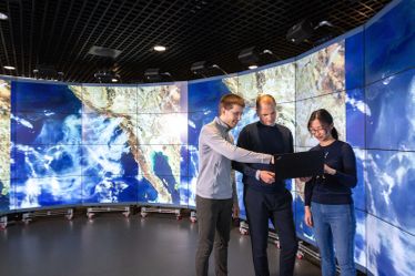 Three people using a laptop in front of screen with high resolution satellite images at the Global Data Observatory in the Data Science Institute.