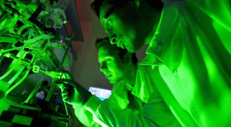 Two researchers fixing bolts and are reflected with luminous green light.