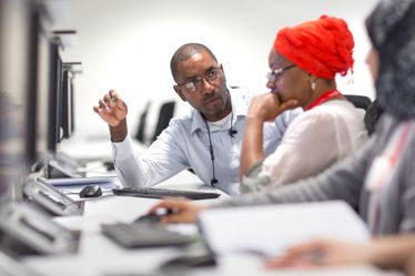 Dr Wayne Mitchell and two students working at computers discuss a problem