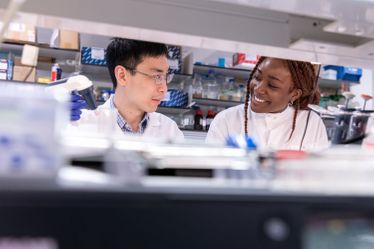 Two researchers smile at each other in white lab coats in the lab