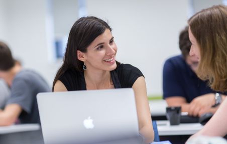 Student on laptop smiling to person to their left