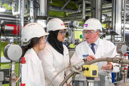 One older male and two younger female professionals in hard hats and white coats talking in an industrial facility