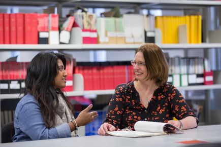 A teacher and a student talking while sitting at a desk with an open book