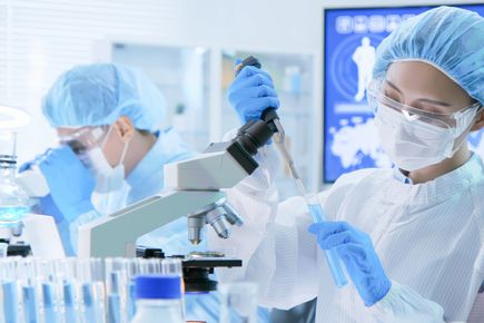 Two lab workers using microscopes and PPE