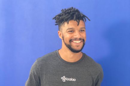 Man in a grey t-shirt smiles at the camera, against a blue background