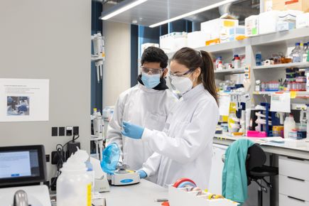 Two students leaning over piece of lab equipment