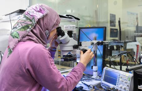 scientist looking into microscope with computing equipment in the background