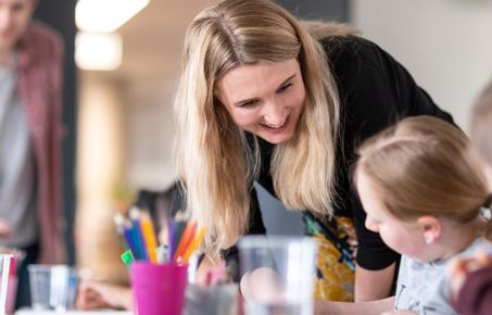 Woman smiling down at child drawing at a table