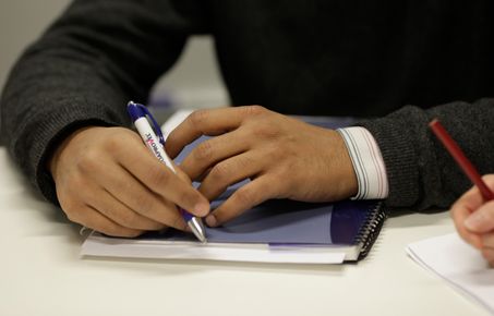 Hand holding a pen and resting on a notebook