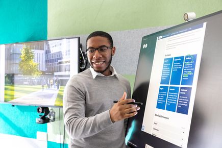 A man smiling and presenting at an interactive screen