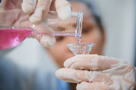 A laboratory worker pouring pink liquid into a glass receptacle