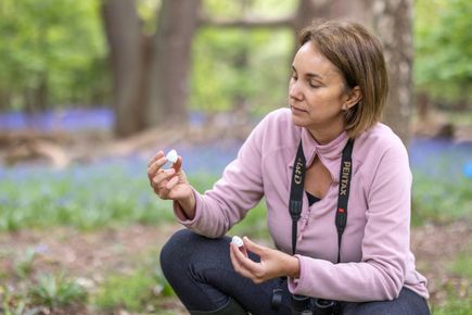 A woman crouches in a forest, looking at a broken eggshell in her hands