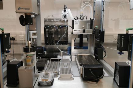 An image of the inside of an automated synthesis platform. The image shows a series of holders for vials and filter tips, a four needle head tool and a gripper tool