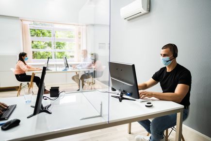 Two people sat at office tables apart from each other, working on laptops and wearing face masks