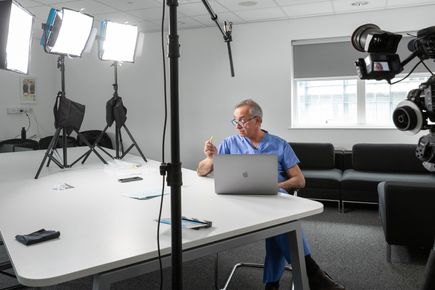 Professor Darzi sits at a table under bright lights, recording an instructional video