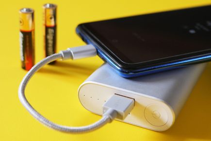 A smartphone connected to a battery pack for recharging. Two AA non-rechargeable batteries are visible in the background