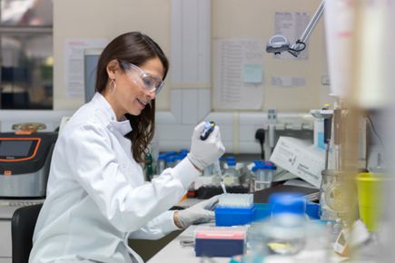 A researcher in a labcoat and safety glasses pipettes