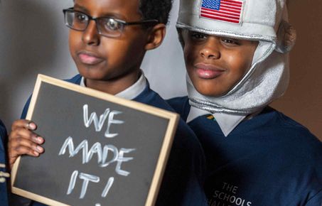 Student holding 'we made it' sign and student in an astronaut helmet