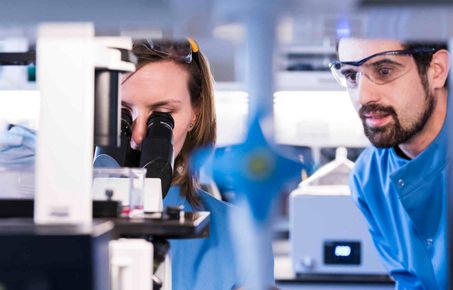 An image of two people looking at findings from a microscope