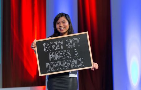 Student smiles holding a blackboard that says 'Every gift makes a difference'.