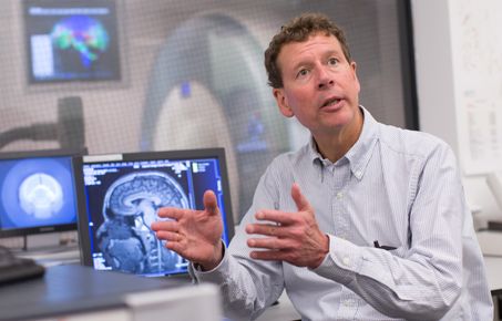 Centre director Paul Matthews sits in front of computer showing brain scan