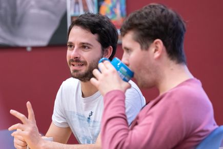 two male students sitting together, one drinking coffee