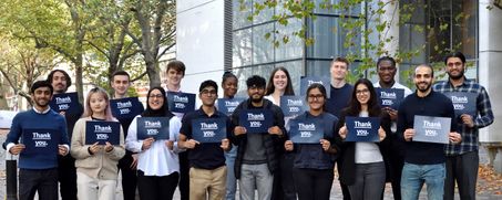 A group of students smile at the camera holding signs that say 'Thank You' and 'Student Caller 2022'