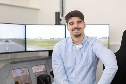 A student sits in the flight simulator, with flight simulation in the background