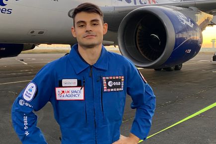 A man in a blue flight suit standing in front of an airplane