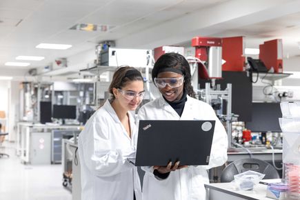 Image of students on in a lab, looking at a laptop.