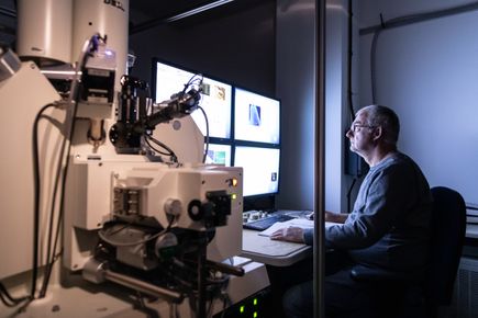 Man sits in front of computer screens in a lab setting.