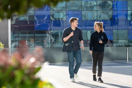 Two students chat and walk through the Dalby Court in the sunshine