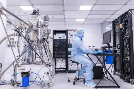 An engineer in a safety suit works at a computer in a lab