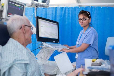 Older male patient in bed with doctor looking at screen