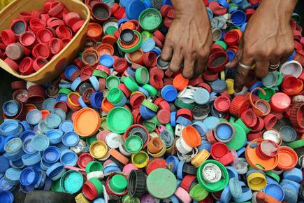 A tub of brightly coloured plastic bottle tops. The hands of an adult are picking out red lids and placing them into a small box