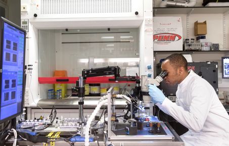 Male PhD student in a lab looking through a microscope