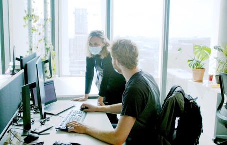 Man sitting at desk working on a computer while woman leans over to chat