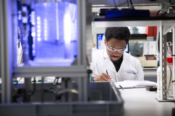 A male in a lab, wearing a lab coat and making notes on paper