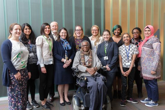 A diverse group of graduates smile at the camera gathered behind Ossie Stuart a black wheelchair user who has lead their course