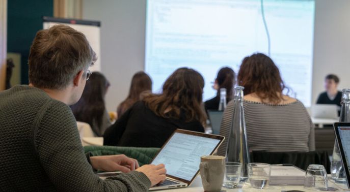 Man sitting at desk and typing on his laptop listening to the speaker at a seminar 