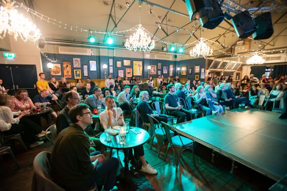 Crowded audience sit opposite a small stage in a pub