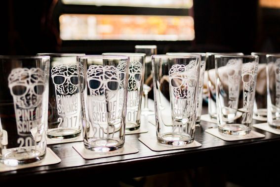 Several pint glasses lined up on a bar with Pint of Science logo engraved on them